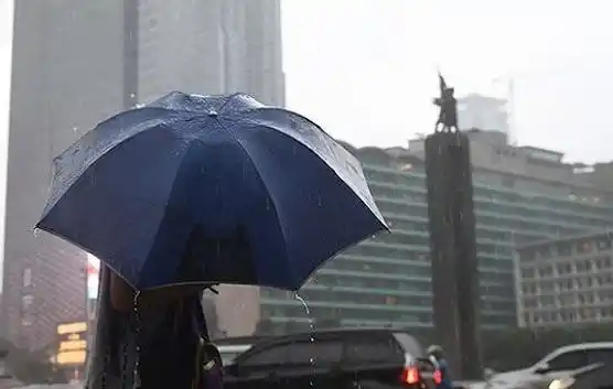 Seorang mengenakan payung hujan sedang melintas di kawasan Bundaran Hotel Indonesia (HI) (Foto: Istimewa)