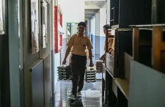 Seorang siswa sedang mengantarkan makanan MBG