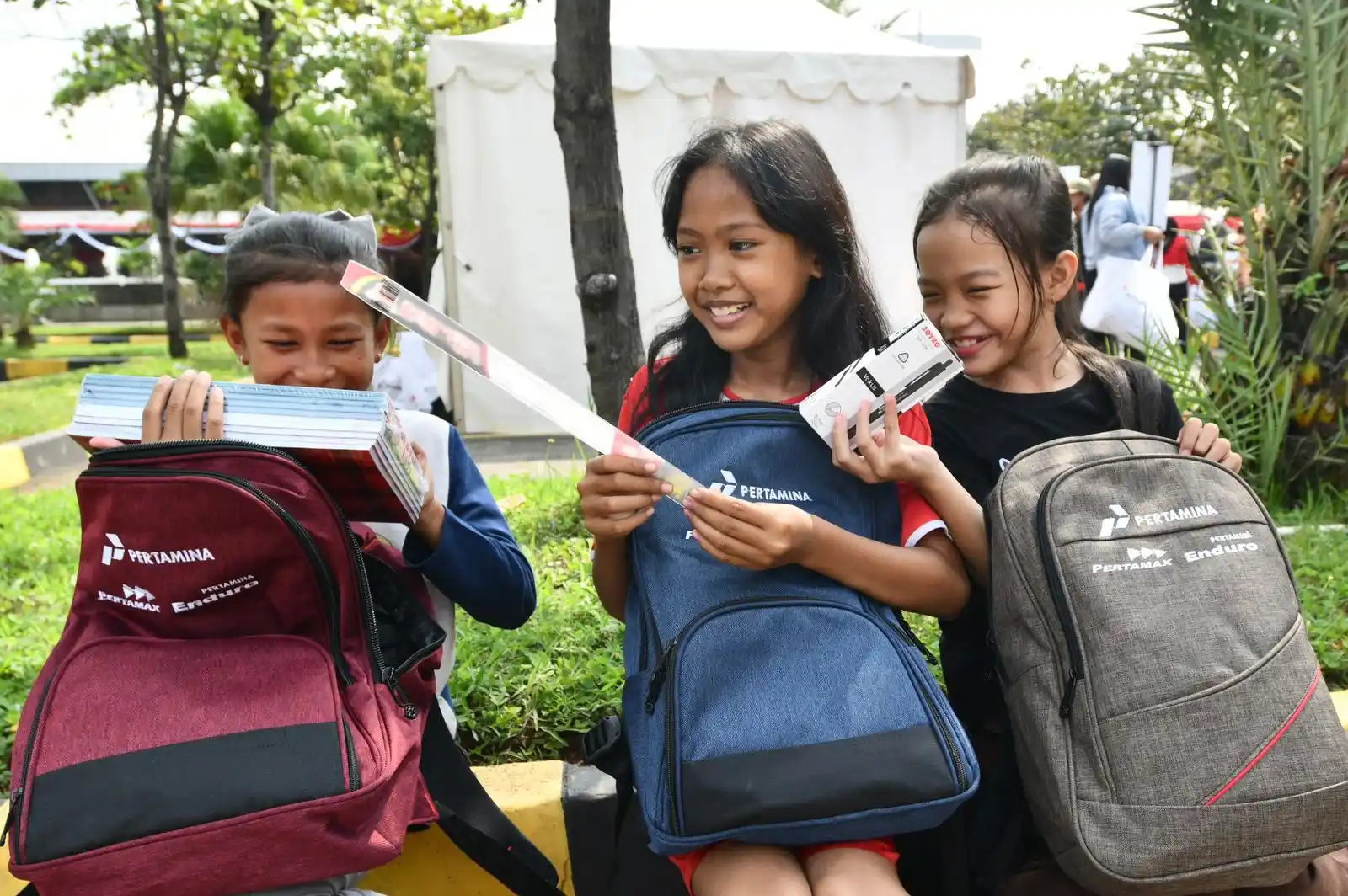 Tiga Siswa menunjukkan isi tas yang dibagikan saat acara SESAMA Seribu Seragam Sekolah Bersama Pertamina yang diselenggarakan di Kantor Pertamina LOBP & Grease Plant - Production Unit Jakarta (PUJ) Koja, Jakarta Utara, pada Kamis (14/8/2025). [Foto: Doc. Pertamina]